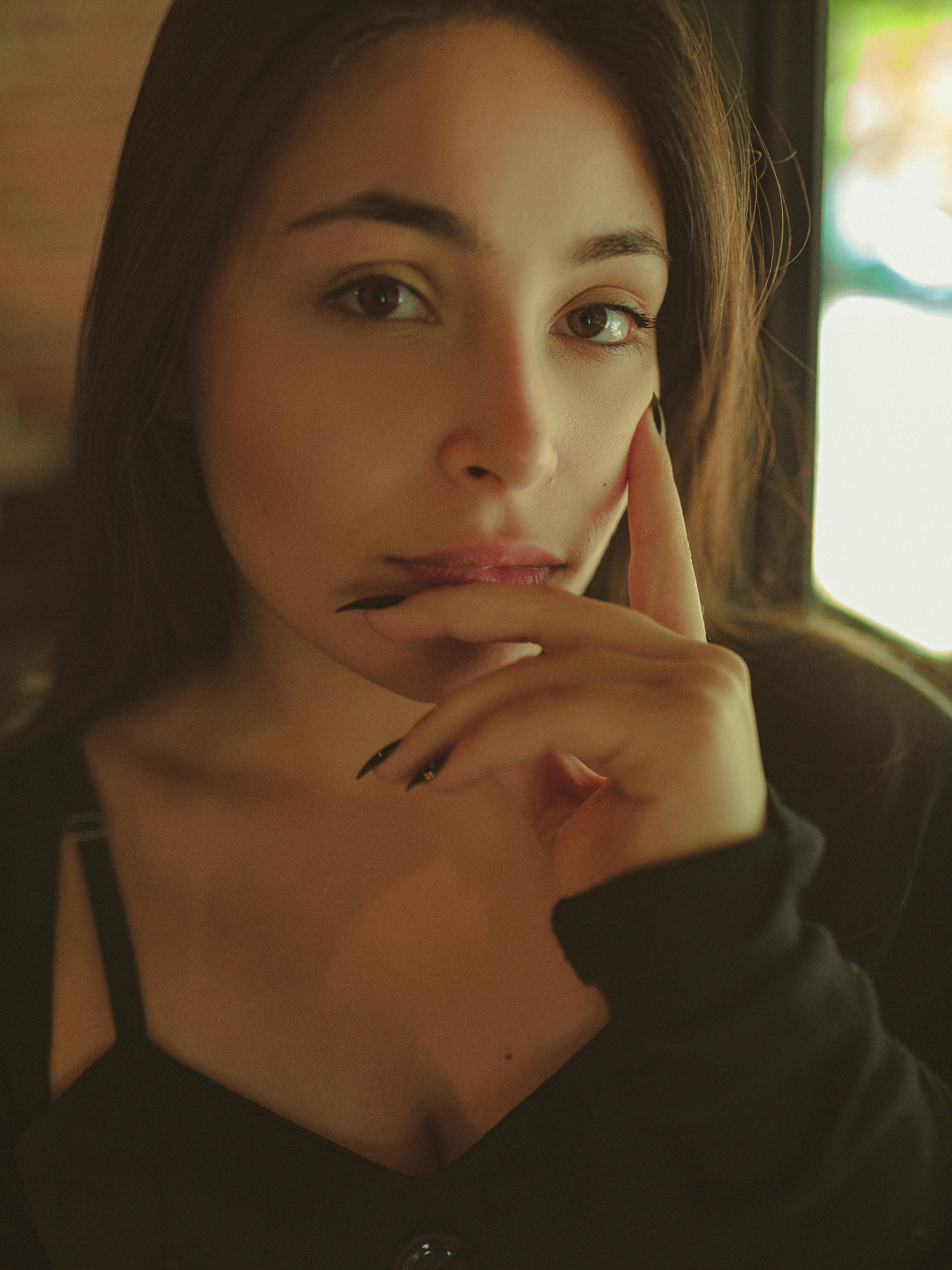 一位身着黑色上衣的年轻女子，在室内若有所思的特写肖像