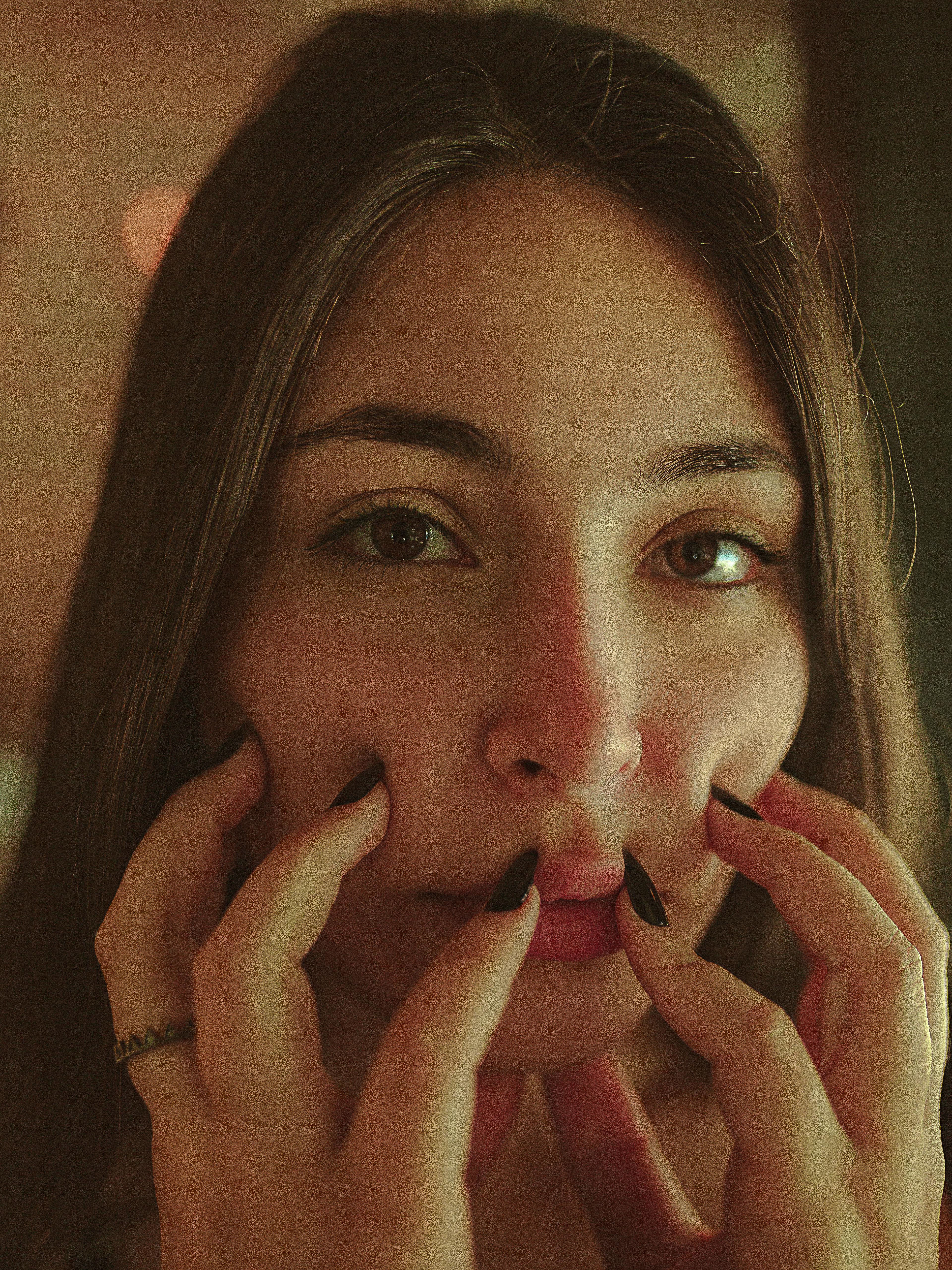 一幅亲密特写肖像，描绘了一个女人用修剪整齐的指甲轻触自己的脸庞