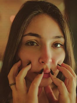 一幅亲密特写肖像，描绘了一个女人用修剪整齐的指甲轻触自己的脸庞