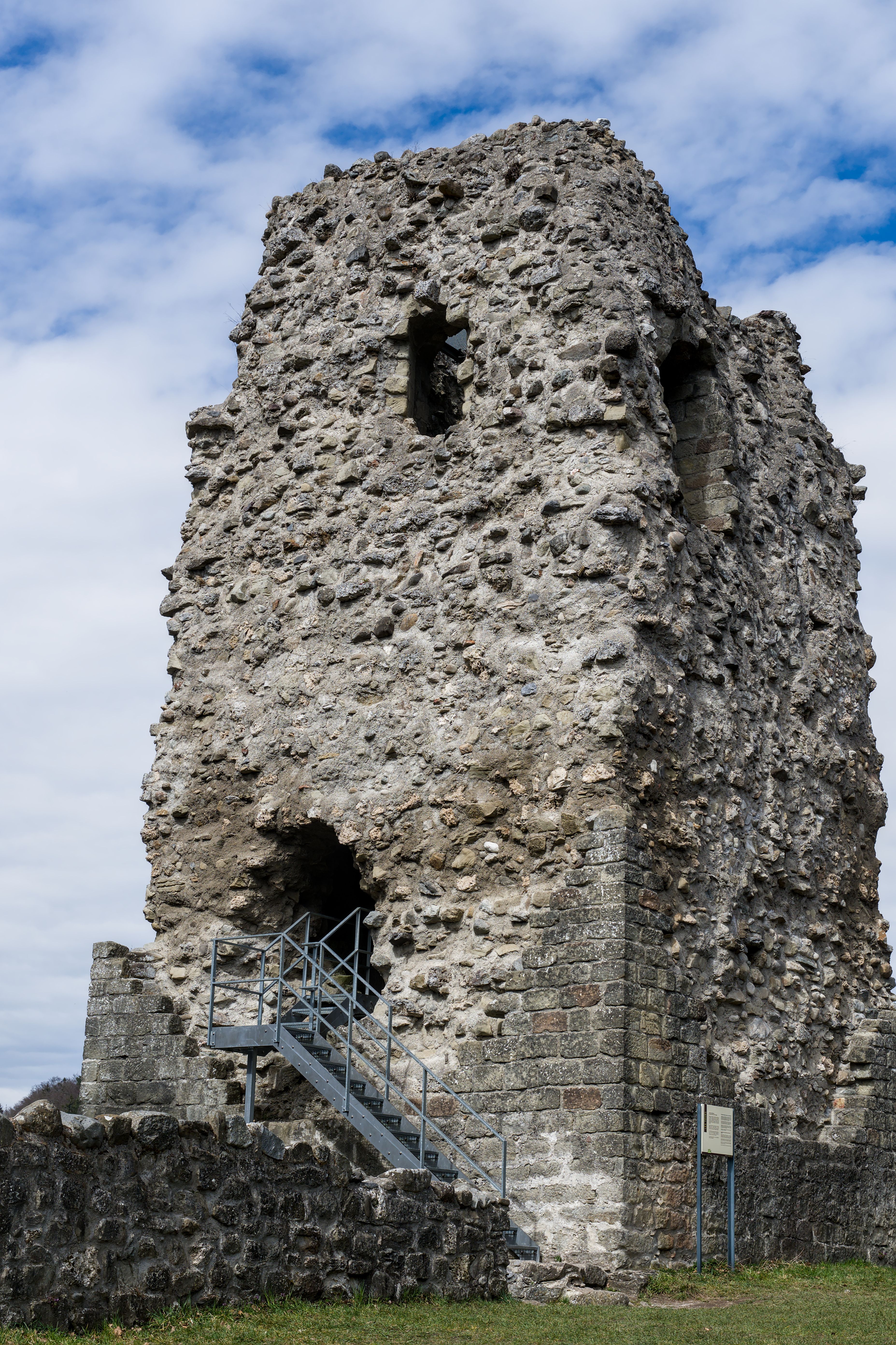 Ancient stone tower remains with steps leading up, captured under a bright sky in Switzerland.