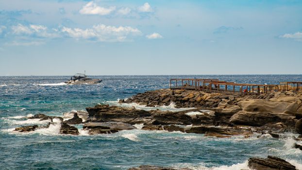 A boat sails along the rocky coastline of Sanremo, Liguria, Italy on a sunny summer day.