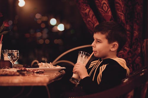 Boy Holding Drinking Glass Sitting in Front of Table
