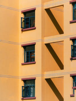 A vibrant yellow apartment building with open windows casting shadows.