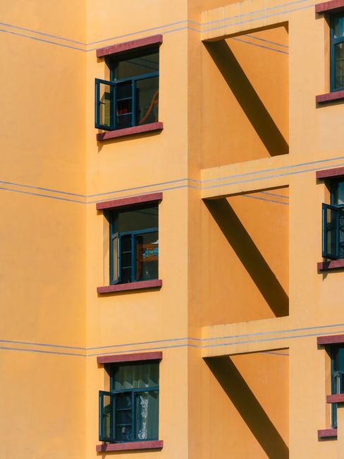 A vibrant yellow apartment building with open windows casting shadows.