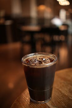 Chilled iced coffee in a plastic cup on a wooden table indoors with blurred background.