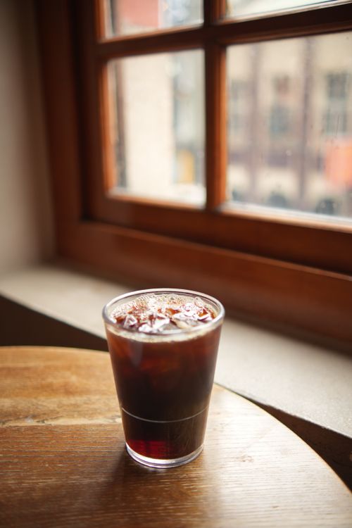 Free Chilled iced coffee in a glass on a cozy wooden table by a window. Perfect for cafe vibes. Stock Photo