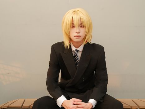 Young adult with blonde hair in a suit seated indoors. Neutral background.