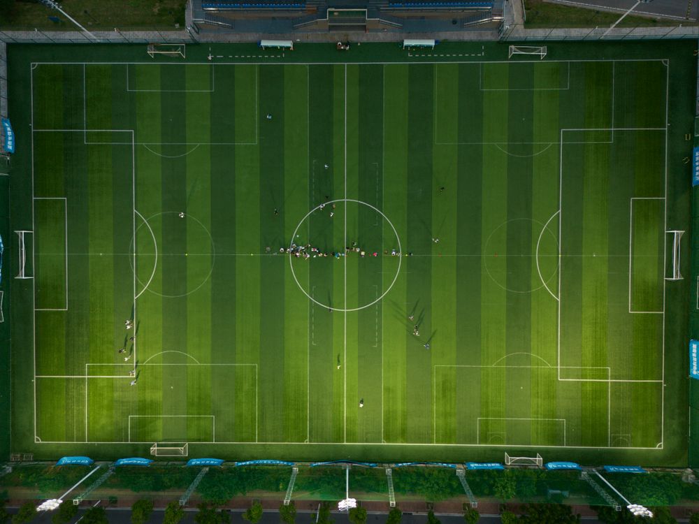 Top-down aerial view of a soccer field with players positioned during a daytime match