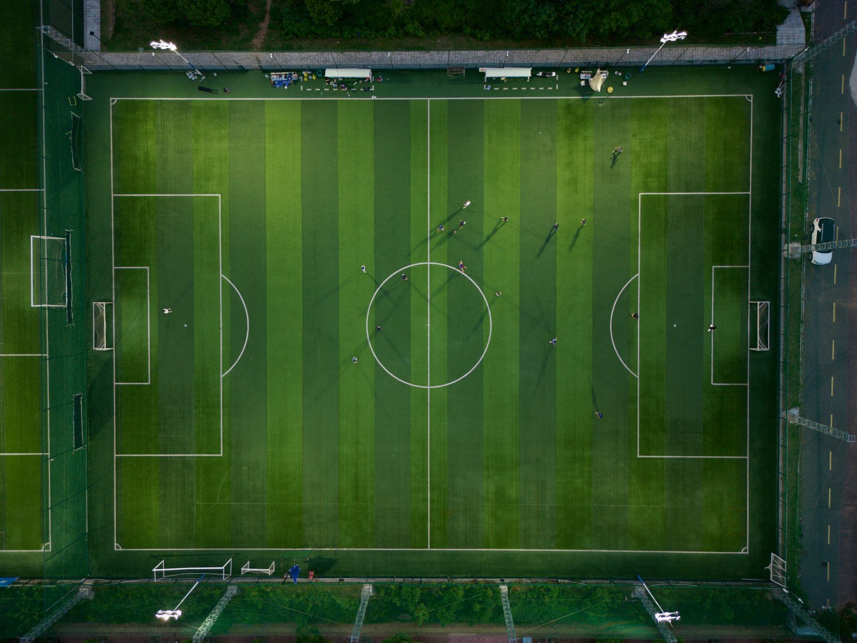 Top-down view of a soccer field with players during a match, casting shadows.