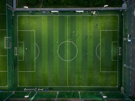 Top-down view of a soccer field with players during a match, casting shadows.
