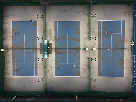 Aerial shot of three tennis courts with players during the day.