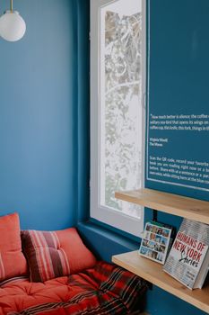 A cozy reading nook with blue walls, cushions, and books by a window overlooking nature.