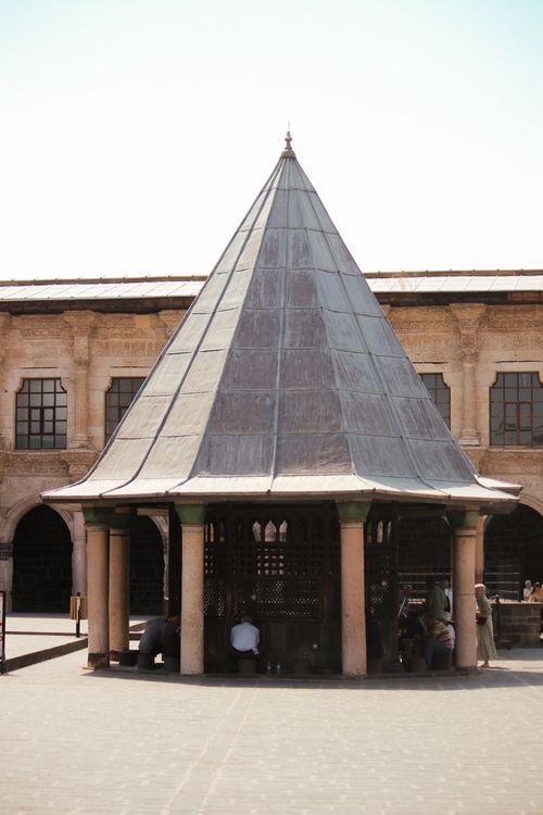 Free A historic building with a conical roof in a sunlit courtyard. People are sitting underneath. Stock Photo