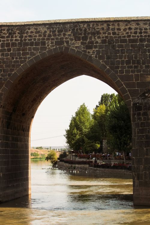 Free A picturesque view of an ancient stone bridge arching over a calm river surrounded by lush greenery. Stock Photo
