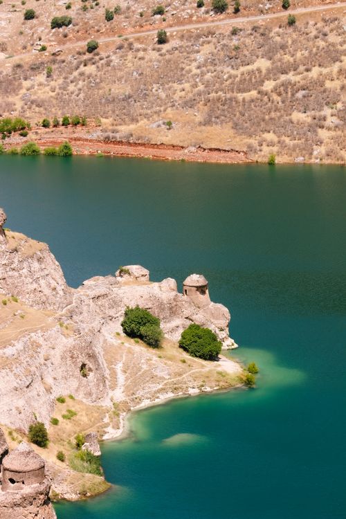 Free Serene landscape of ancient ruins on a cliff by a tranquil, turquoise lake. Stock Photo