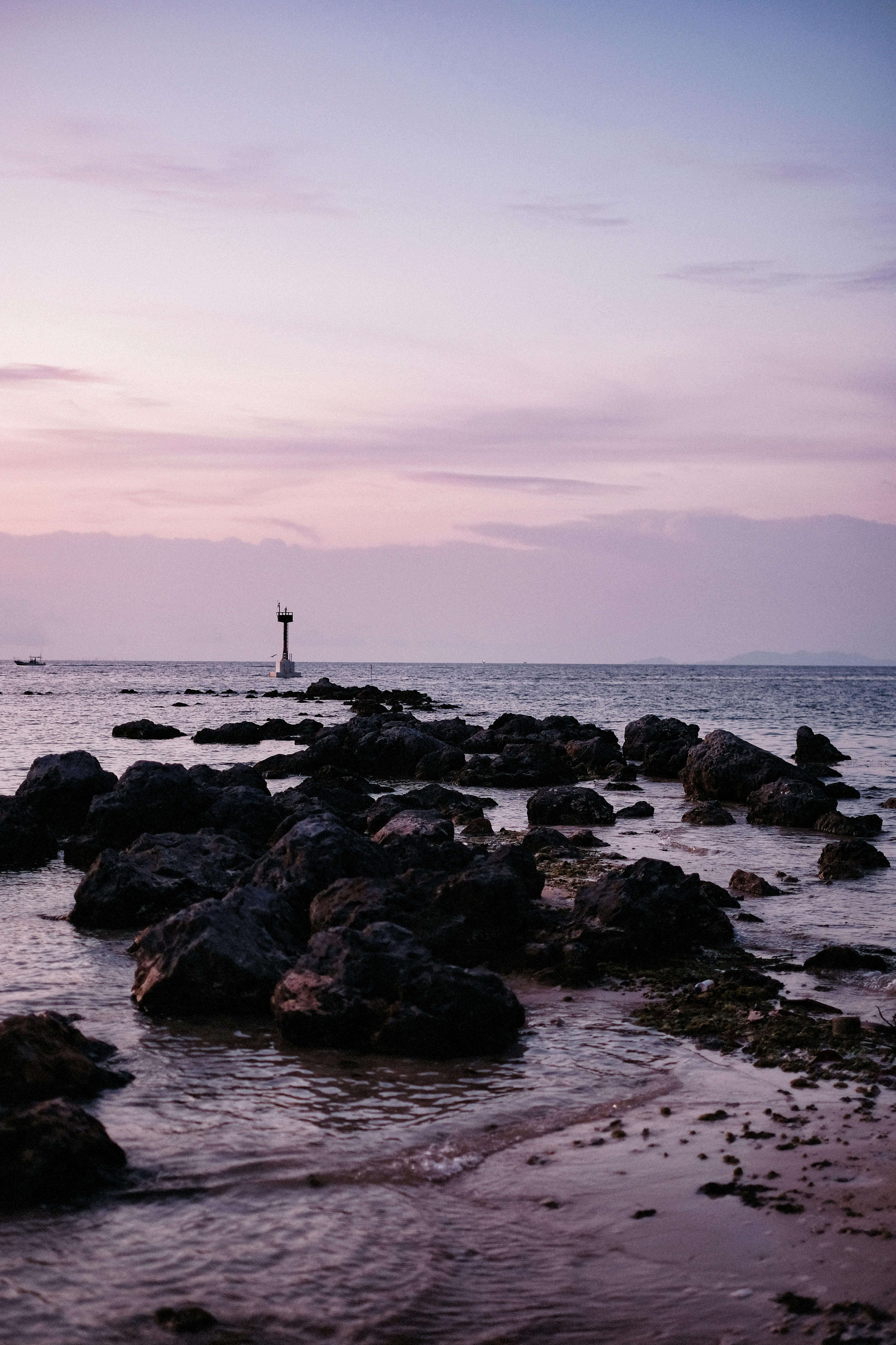 A serene coastal scene with rocky shore and lighthouse at sunset.