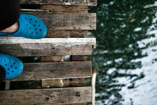 Close-up of feet in blue shoes on a wooden bridge above water.