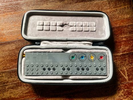 Compact synthesizer inside a cushioned case on a wooden surface.