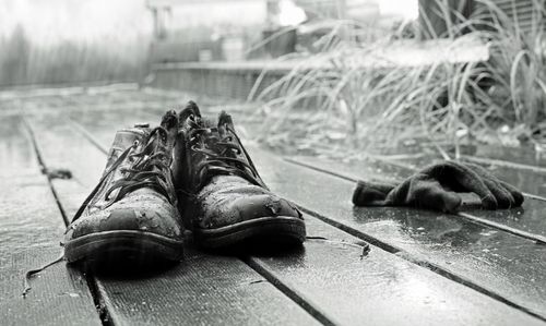 Free Black and white photo of wet shoes and gloves on a rainy wooden deck, conveying solitude. Stock Photo