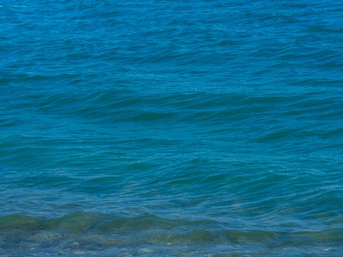 Free Gentle ocean waves under a clear blue sky creating a soothing and tranquil scene. Stock Photo
