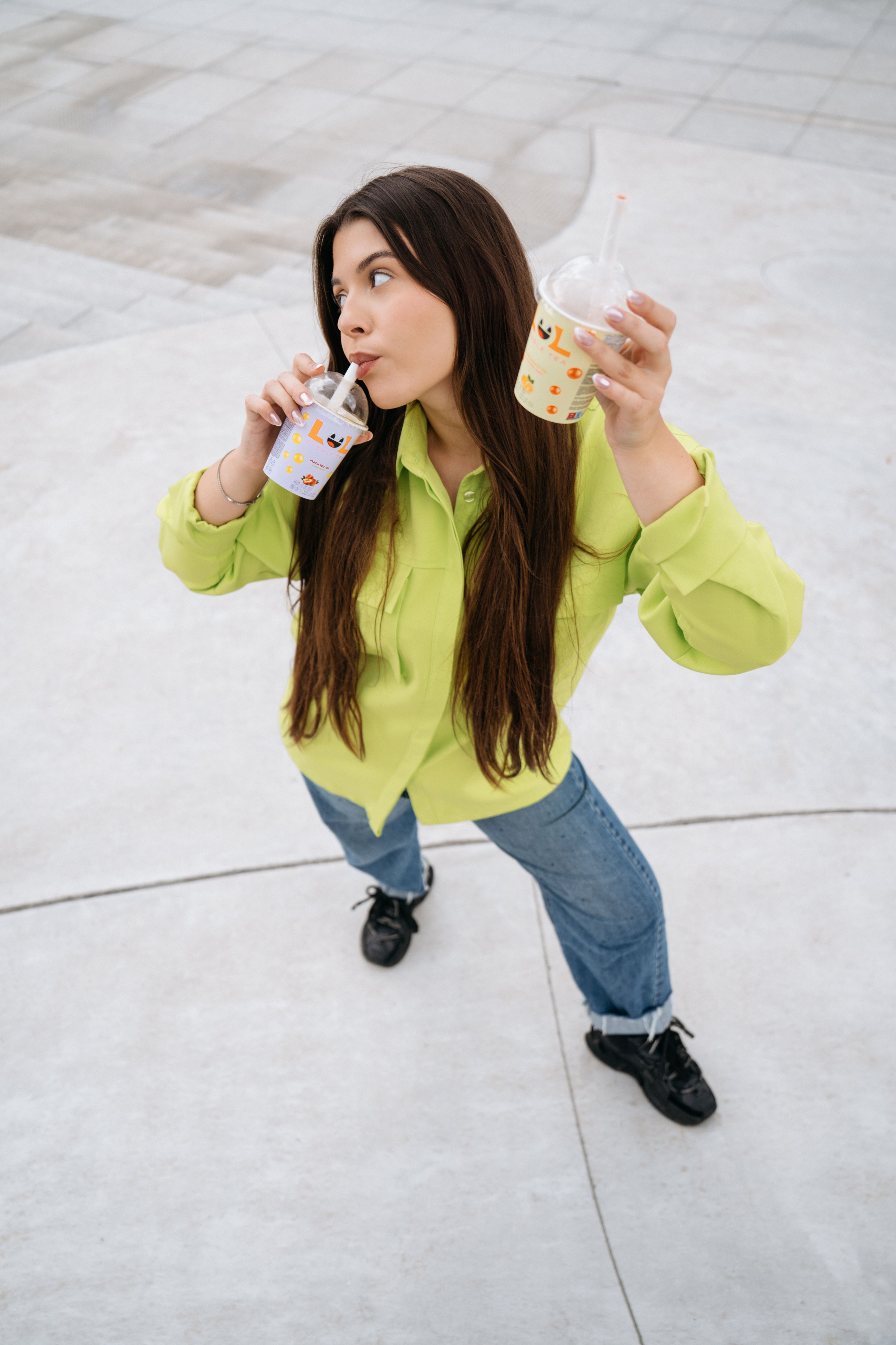 Stylish young woman holding two bubble teas in an urban outdoor setting.