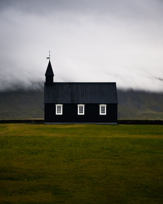 Stark black church against cloudy Icelandic landscape.