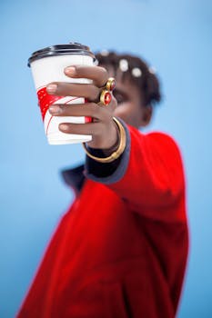 Stylish individual in red jacket holding coffee cup with blurred face.