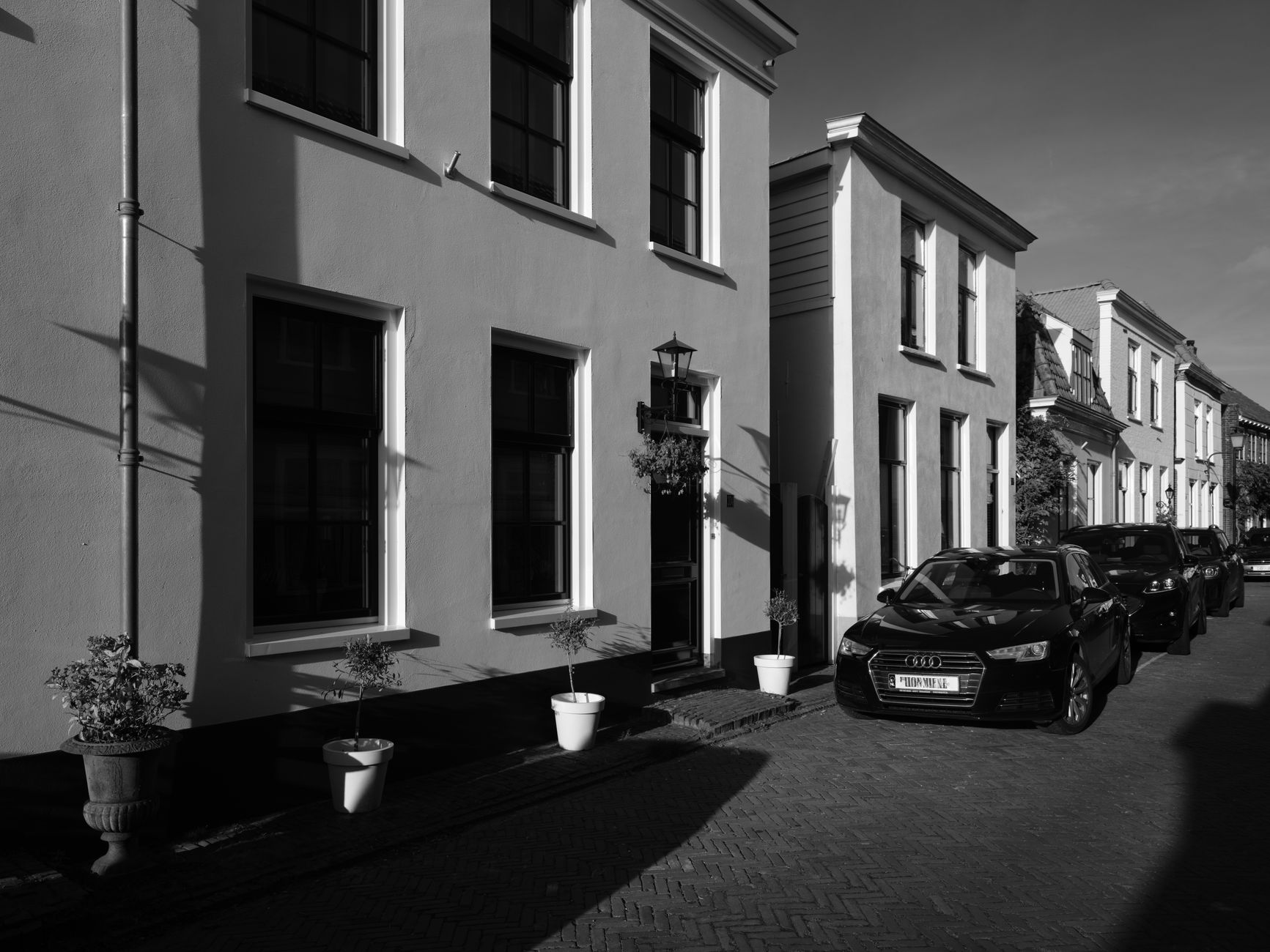 A black and white photo of charming houses with parked cars on a sunlit street.