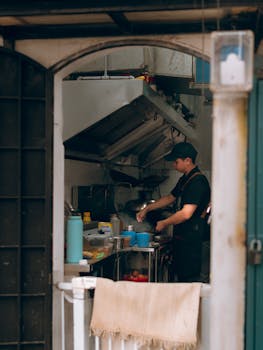 A chef cooks in a cozy restaurant kitchen, seen through a doorway.