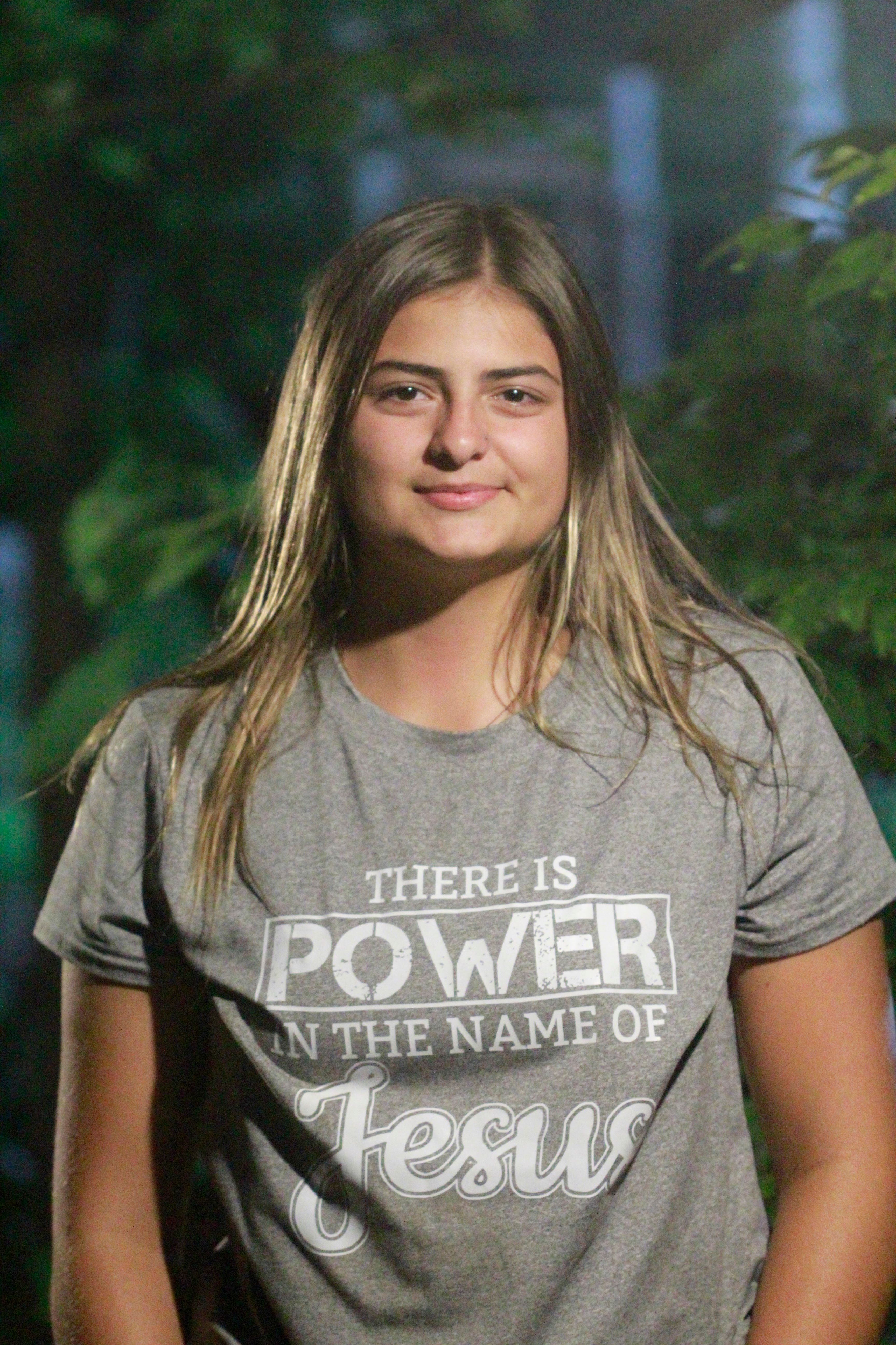 Young woman outdoors wearing a shirt with an inspirational message about faith.