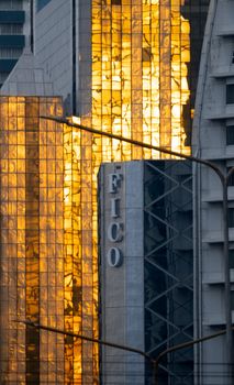 A vivid cityscape featuring a sunset reflection on the modern glass facade of FICO building in Bangkok, Thailand.