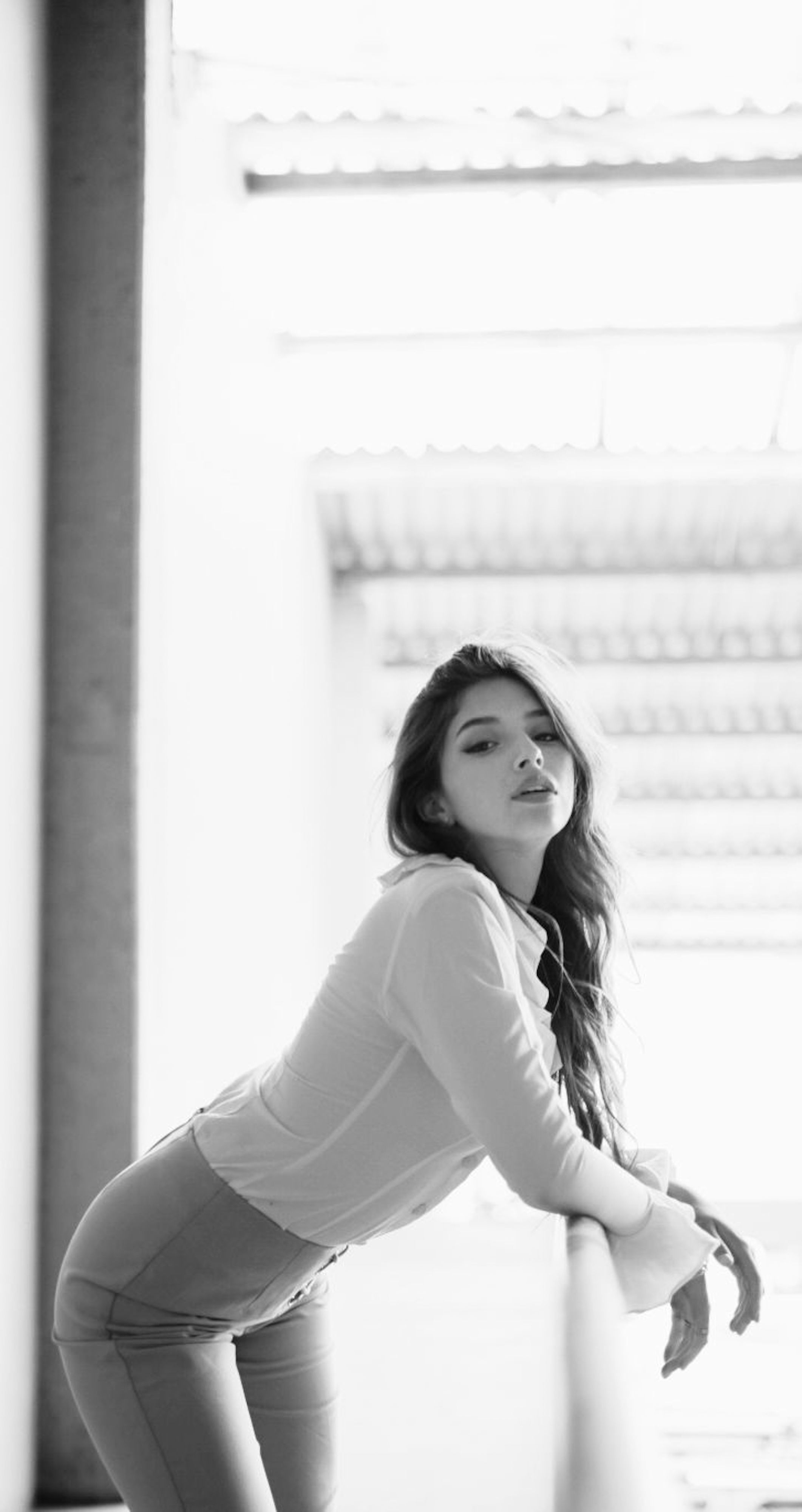 Elegant black and white portrait of a woman leaning against a railing, showcasing modern style.