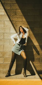 A fashionable woman strikes a pose against a sunlit brick wall, exuding confidence and style.