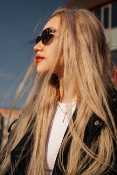 Fashionable woman with blonde hair and sunglasses in sunlight, showcasing edgy style.