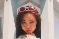 Optimistic tender female with puffed out cheeks and sunglasses on head looking out space between wooden balks and leaning on hand in daylight