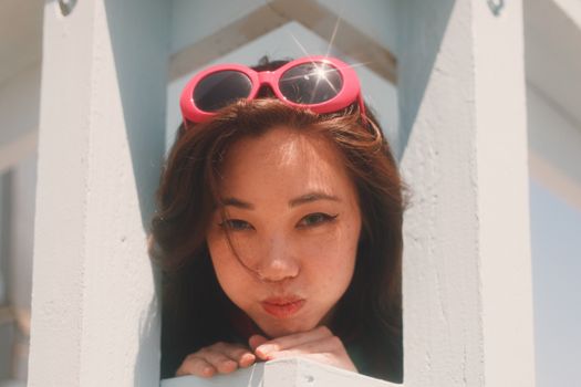 Optimistic tender female with puffed out cheeks and sunglasses on head looking out space between wooden balks and leaning on hand in daylight