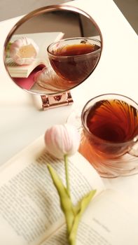 Aesthetic tea setup with tulip, book, and mirror reflection in warm lighting.