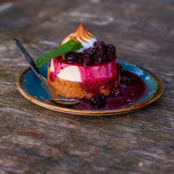Scrumptious blueberry tart with meringue, mint, and coulis on rustic table.