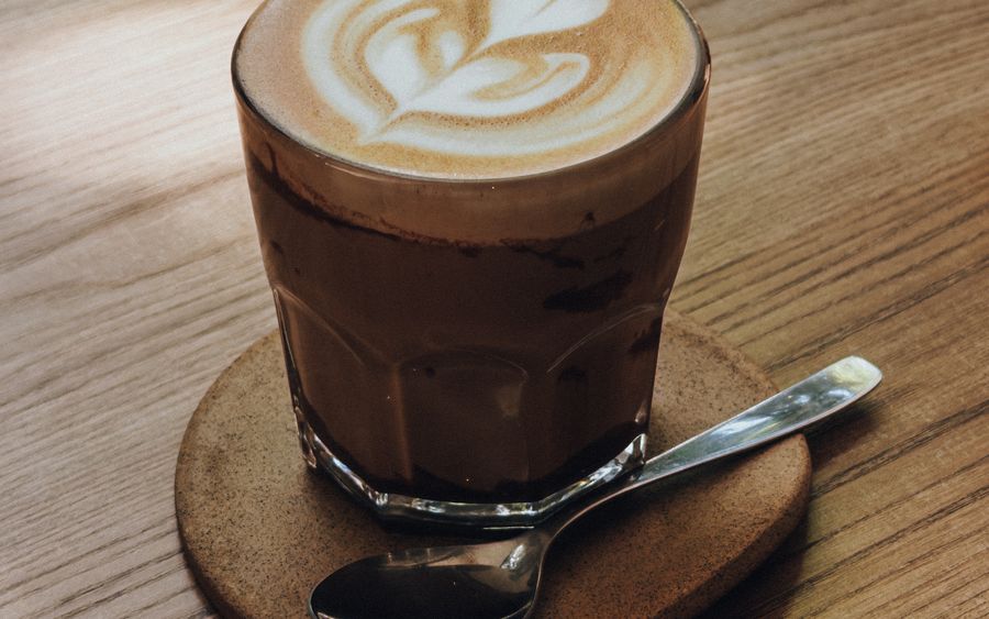 A latte in a small glass with leaf latte art, on a wooden table