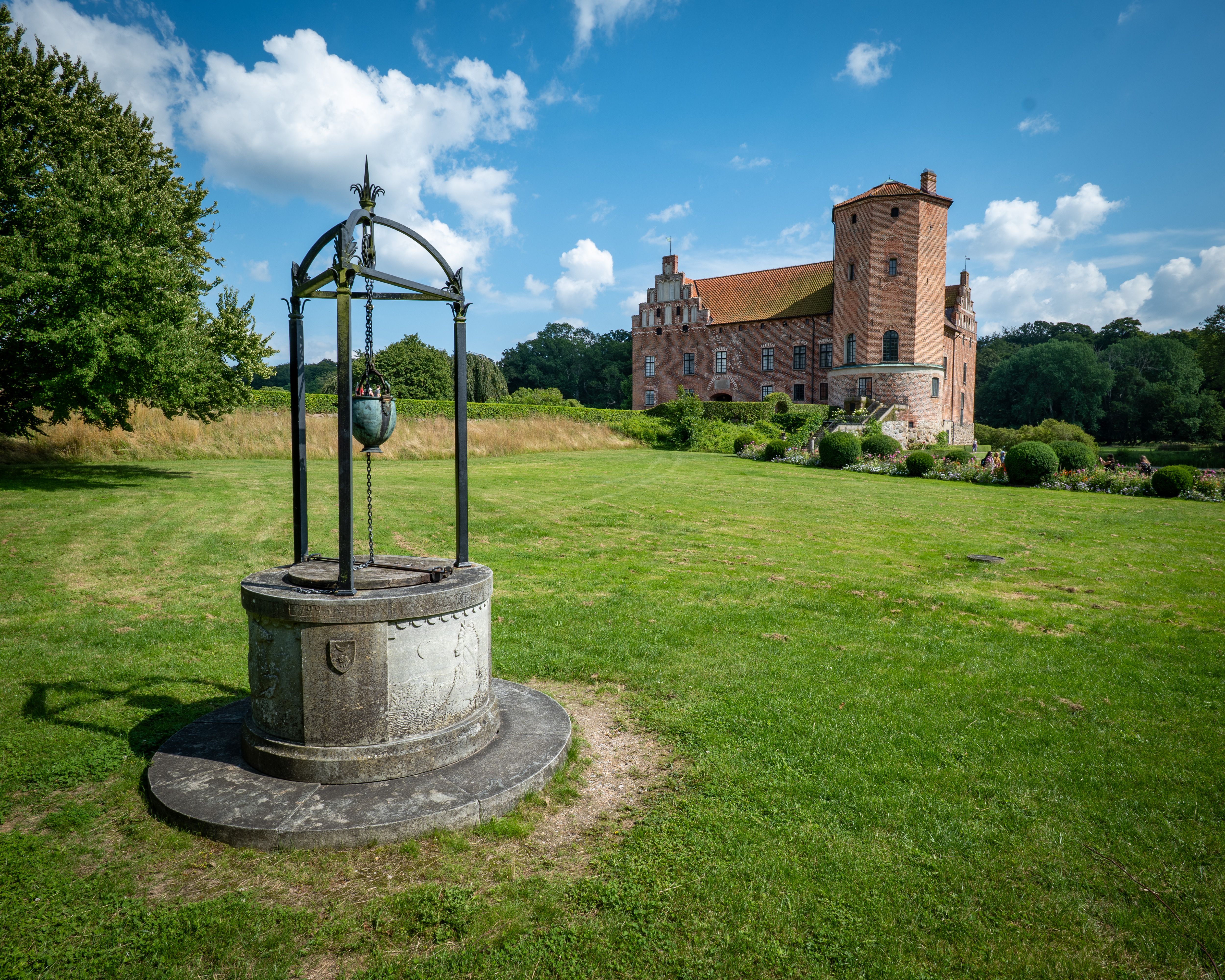 Historical castle with lush gardens and a well, set in scenic Skåne, Sweden.