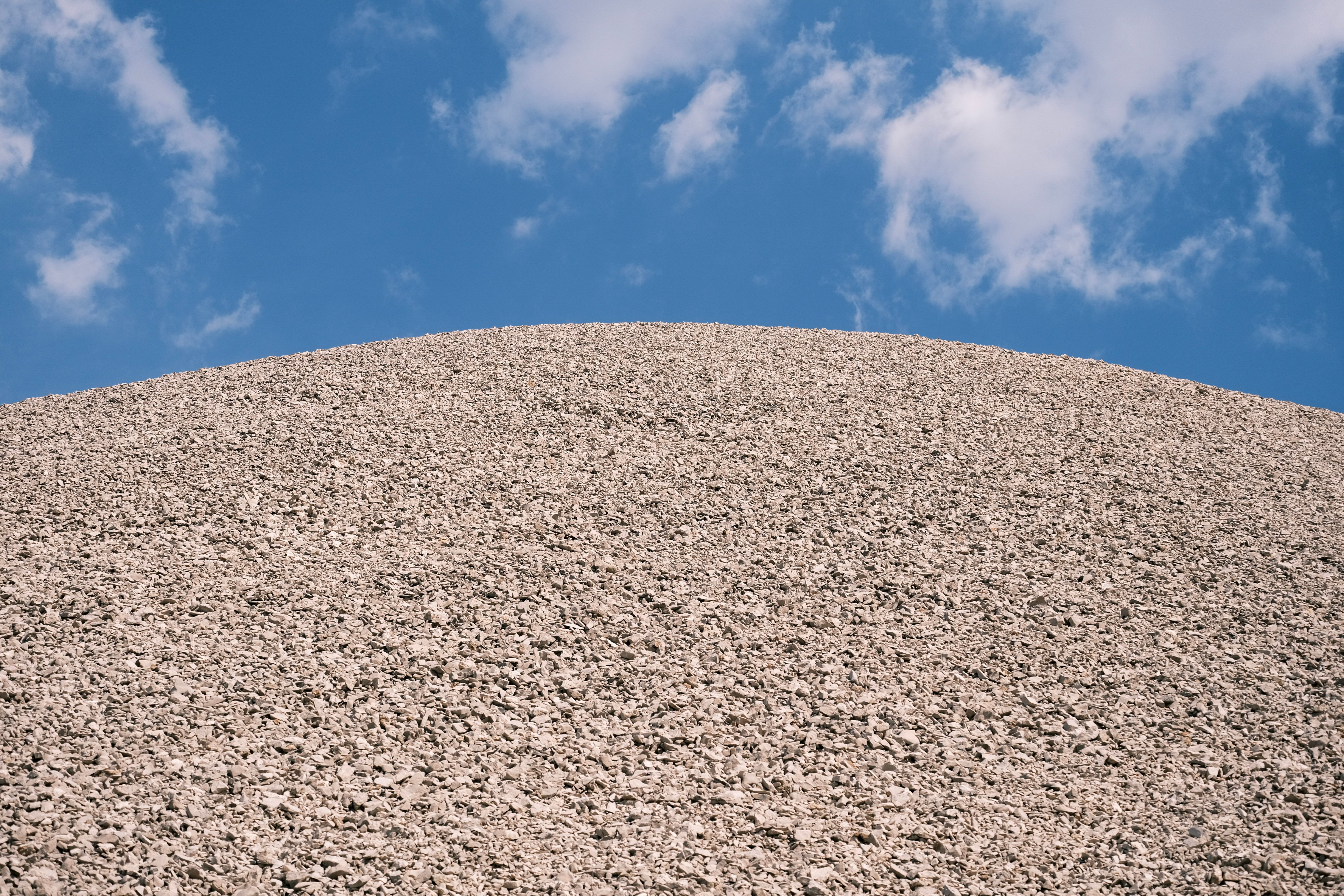 A vast gravel hill with a clear blue sky and scattered clouds overhead, showcasing contrast and texture.