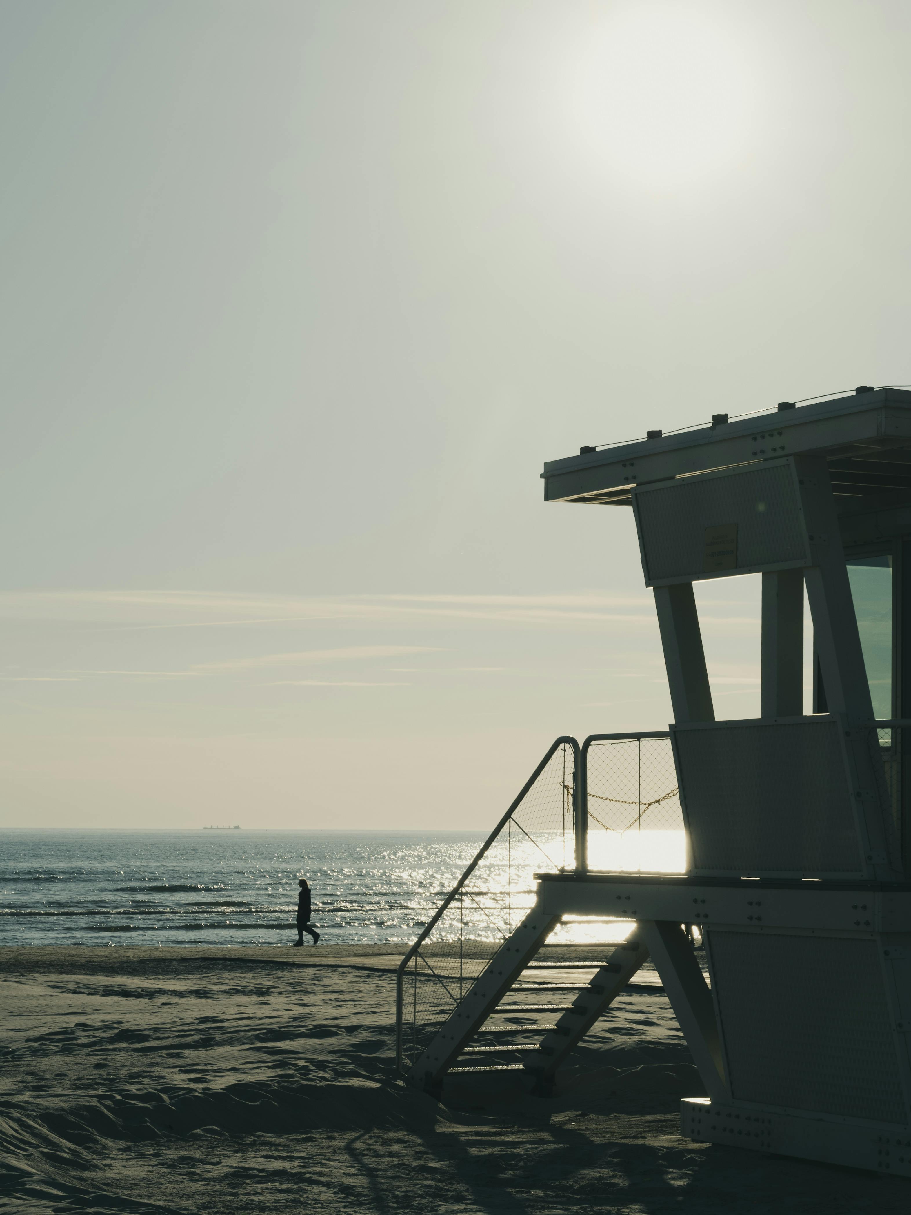 A serene beach scene featuring a lifeguard tower and a lone walker during sunset.