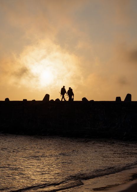 Silhouetted figures walking along a seaside breakwater during a vibrant sunset.