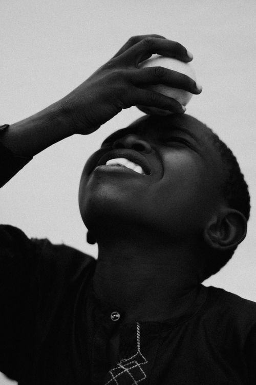 Free Black and white photo of a child smiling, pressing an egg to the forehead, capturing joy and playfulness. Stock Photo