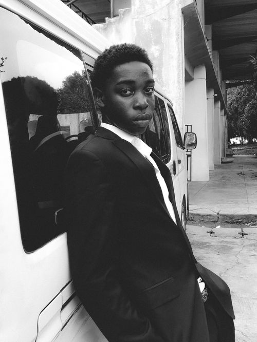 Free Young man in a suit leaning against a vehicle in an outdoor setting, captured in black and white. Stock Photo