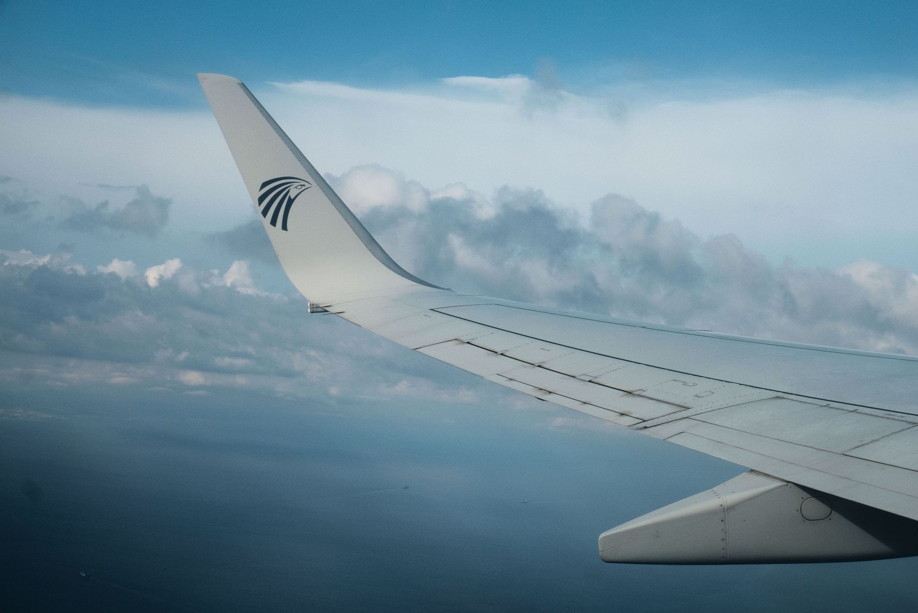 A serene view of an airplane wing cruising over fluffy clouds at high altitude.