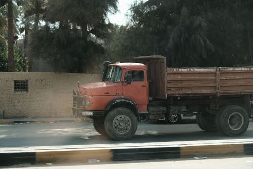 Free A vintage red Mercedes truck navigates a sunlit Cairo street with palm trees in the background. Stock Photo