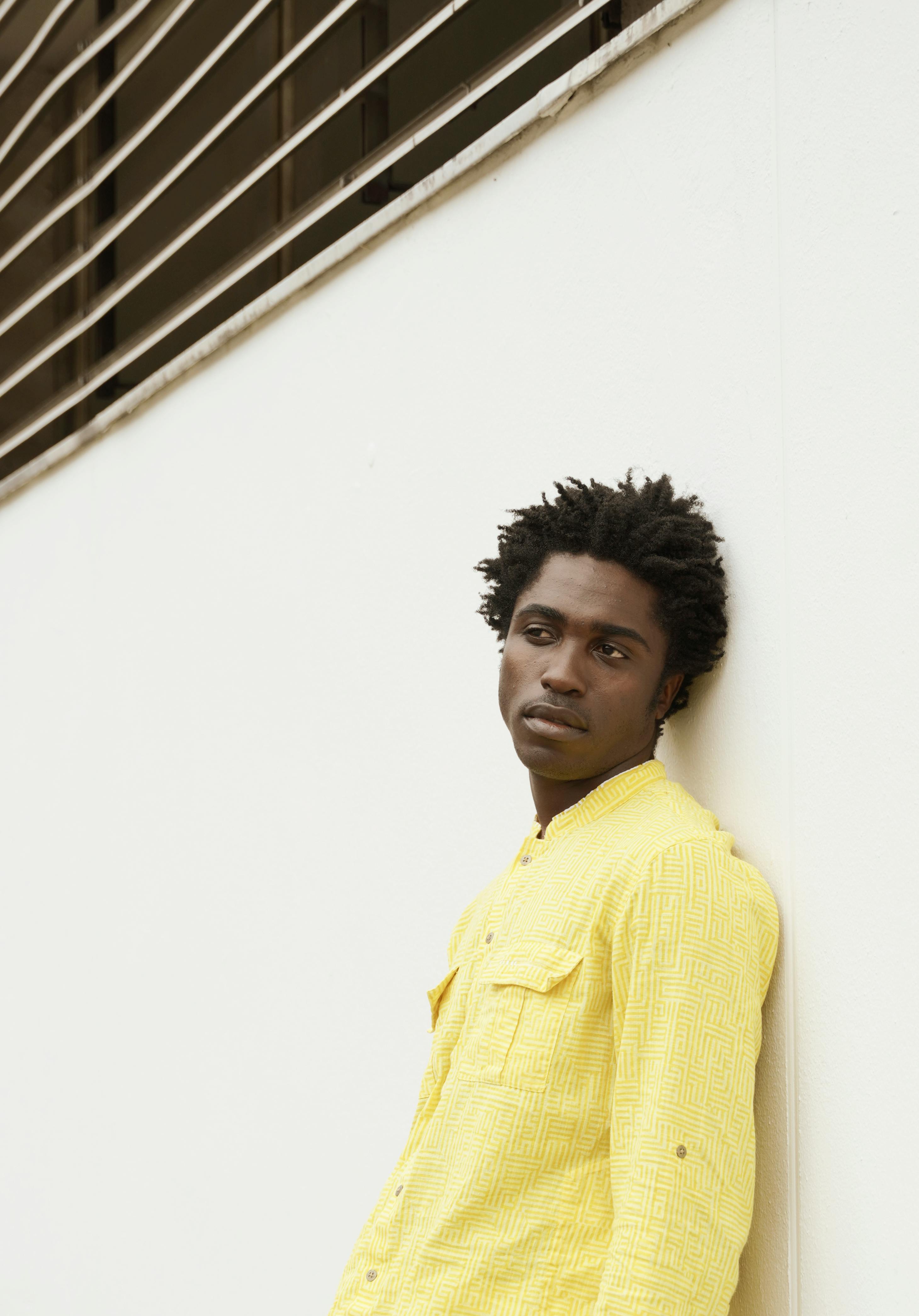 Free Elegant portrait of a man in yellow shirt leaning against a minimalist wall in Berlin. Modern fashion statement. Stock Photo