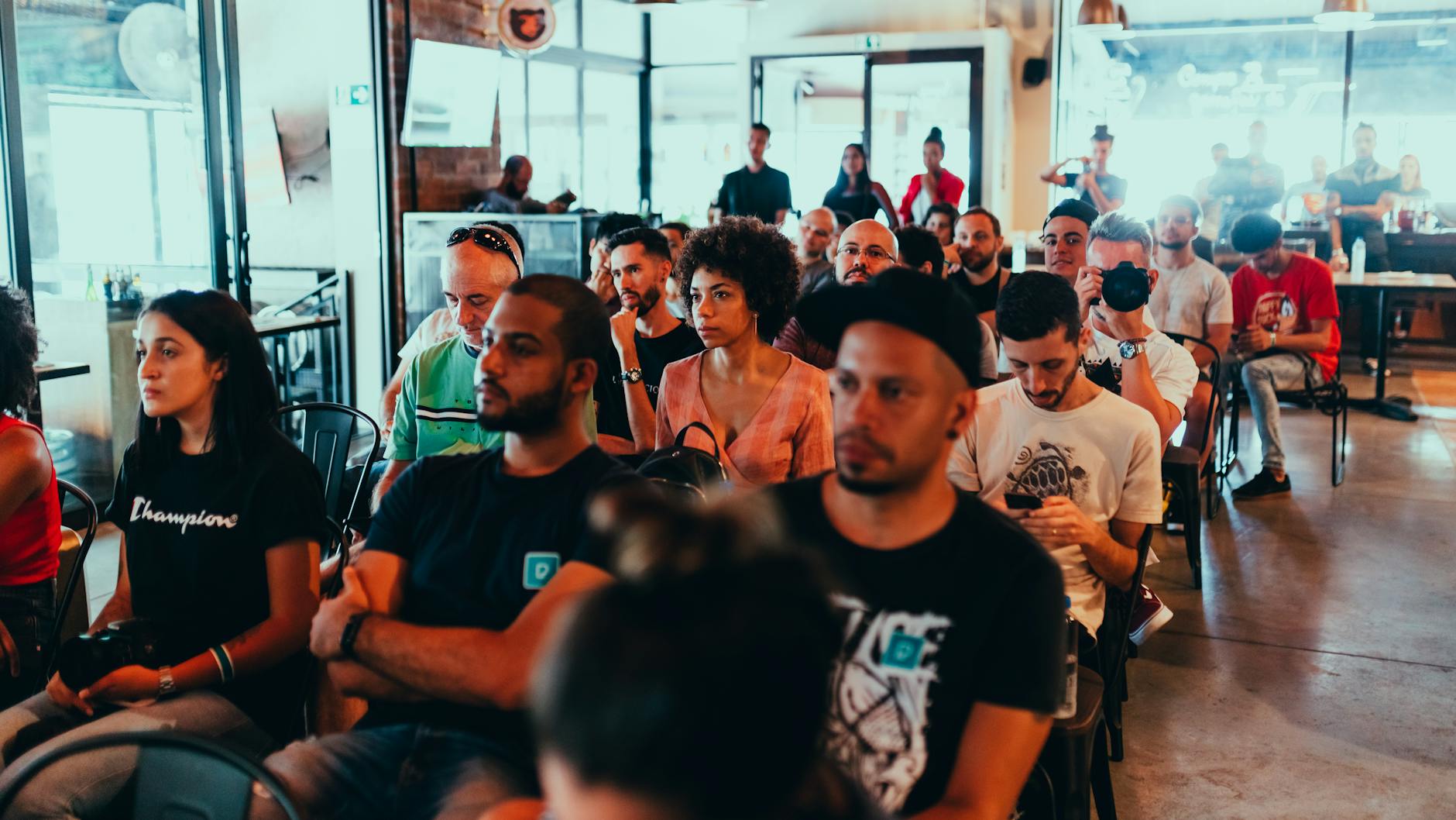 A diverse group of adults attentively participating in an indoor seminar or conference. Alt: professionals reviewing Micro Skills takeaways to learn in a week