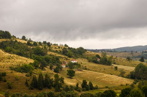 Free Beautiful grassy hills and scattered houses under a cloudy sky in Kosovica, Serbia. Stock Photo